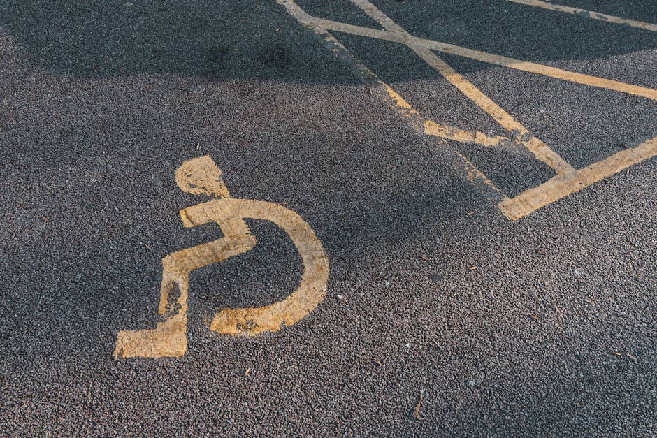 A blue parking sign with a white letter 'P' is mounted above a white sign featuring a black wheelchair symbol, indicating accessible parking. The signs are situated outdoors against a background of le